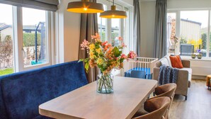 A modern living room with a wooden table, blue sofa, and a vase of flowers. - Holiday Home in Noordwijk Near the Beach (Noordwijk)