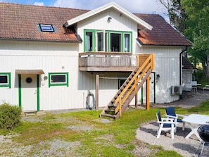 A white building with green trim, a wooden staircase, and outdoor seating.