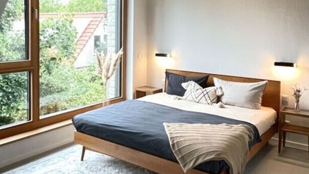 Ein modernes Schlafzimmer mit einem großen Bett, einer Hängelampe und Blick ins Freie.