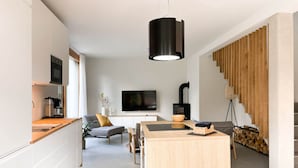 Eine moderne Küche mit Einbauofen, Essbereich mit Kochinsel, Sofa und an der Wand montiertem Fernseher.