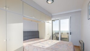 Un dormitorio con cama, armario, puerta corrediza de vidrio a un balcón e iluminación en el techo.