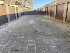 A paved walkway with a brick pattern, flanked by buildings with large garage doors and a brick wall in the center. - Apartment on the Seventh Floor With sea View (Middelkerke)