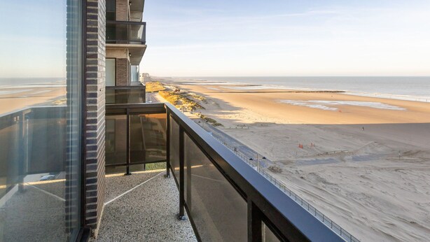Un edificio moderno con un balcón de cristal que da a una playa.