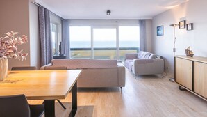 Una sala de estar moderna con una mesa de comedor de madera, dos sofás y vista al mar a través de amplios ventanales.