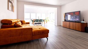 A modern living room with a large sectional sofa, a wooden entertainment unit with a flat-screen TV, and a dining area in the background. - Apartment for 6 Modern Retreat (Andernach)