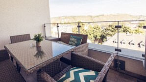 A balcony with wicker furniture, a glass table, and a view of a town and hills. - Apartment for 6 Modern Retreat (Andernach)