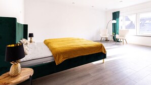 A modern bedroom with a bed, bedside table, lamp, and a view of the city through large windows. - Apartment for 6 Modern Retreat (Andernach)