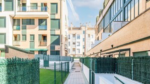 A narrow pedestrian pathway flanked by modern buildings with balconies and windows, leading to a gated entrance. - Apartment in Asturias Near Playa de Torimbia (Llanes)