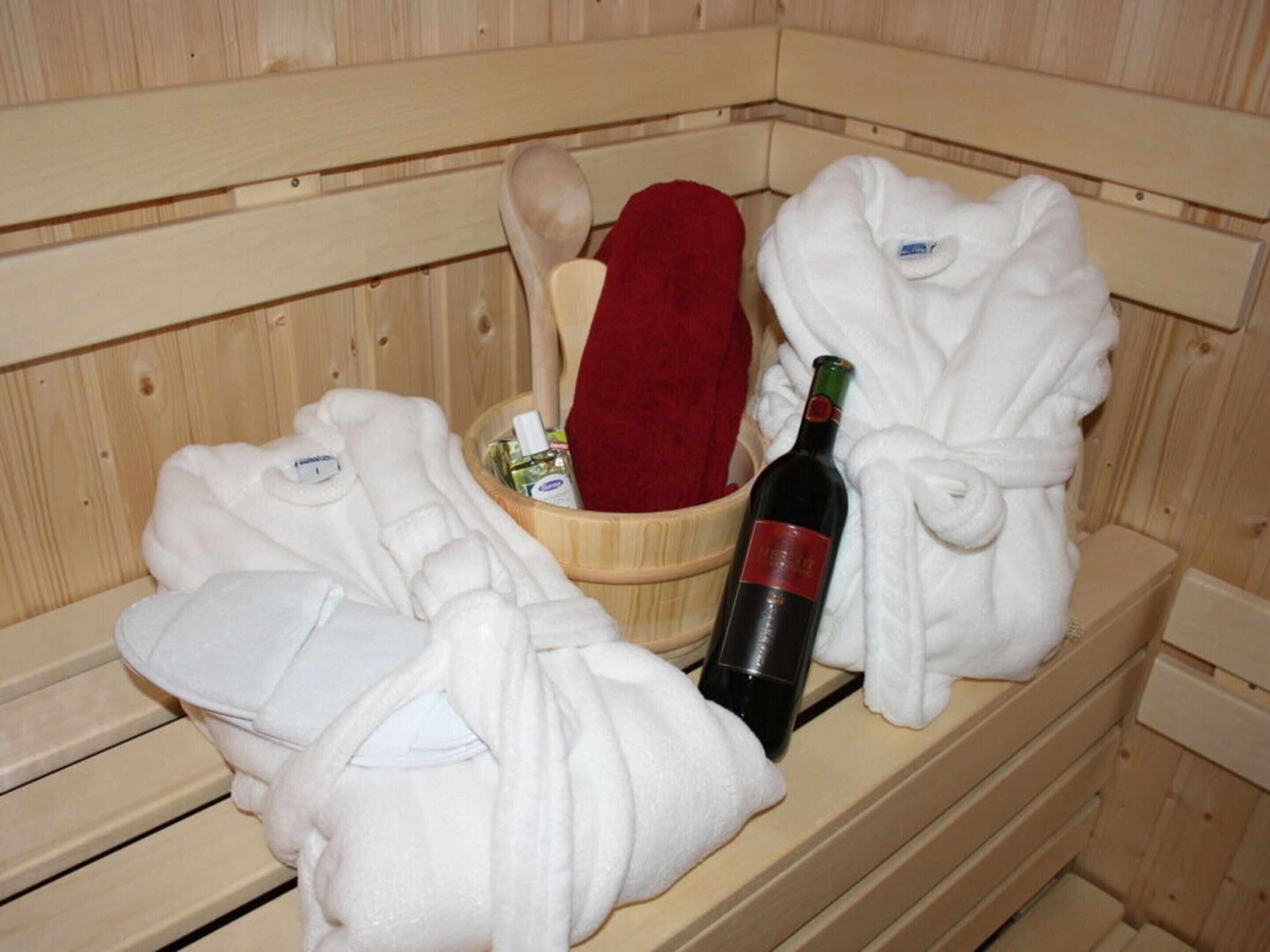 A sauna with wooden benches, a red towel, and a bottle of wine.