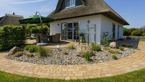 Una casa con techo de paja, un patio con mobiliario exterior y un jardín con rocas y plantas.