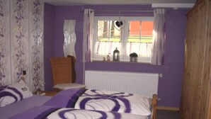 A bedroom with two beds, purple walls, a window with curtains, a radiator, and a wooden wardrobe. - Holiday Home Kobel Comfortable Vacation Home (Elmstein)