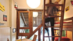 Une pièce chaleureuse avec un lit superposé, une table avec des livres et une fenêtre donnant sur les arbres.