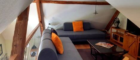 Un espacio habitable estilo loft acogedor, con techo alto, vigas de madera expuestas y un banco de madera integrado.