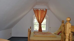 A single bedroom with a wooden bed, a window with curtains, and a radiator. - Holiday Apartment Nature View (Feldberger Seenlandschaft)