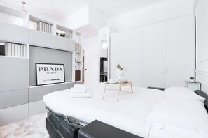 A modern bedroom with a large bed, a bedside table with a vase, and a wardrobe with a Prada sign. - Easylife - Studio apartment in Sant'Ambrogio (Milano)