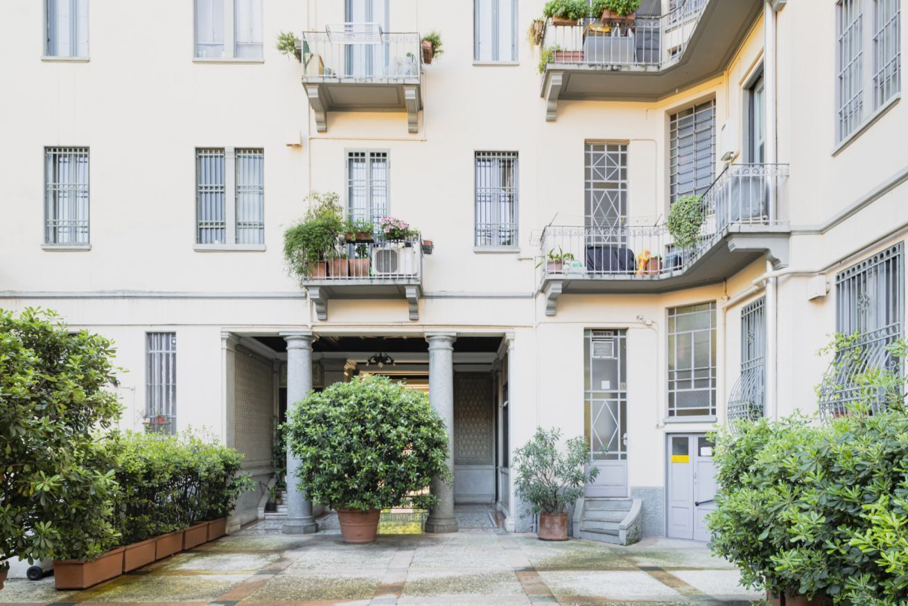 A multi-story building with balconies, potted plants, and a central entrance.