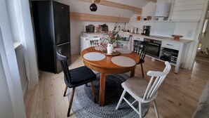 A modern kitchen with wooden beams, a dining area with a round table, chairs, and a refrigerator. - Comfort Steps From the North Sea (Cuxhaven)