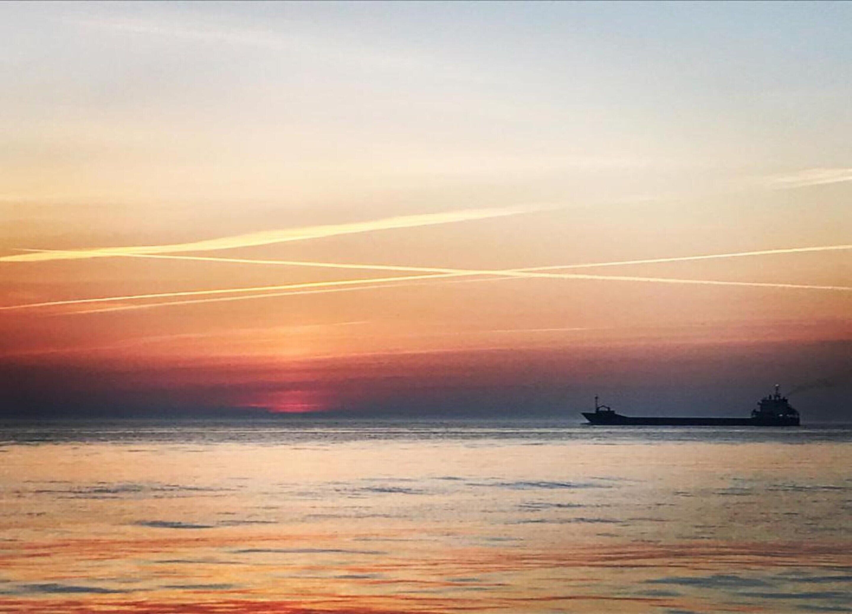 A sunset over a calm sea with a large ship in the distance.