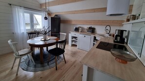 A modern kitchen with wooden beams, a dining area with a round table, and a built-in dishwasher. - Comfort Steps From the North Sea (Cuxhaven)
