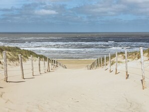 Un sentier de sable qui longe la plage et mène à l’océan, bordé de poteaux en bois et de fil de fer barbelé.