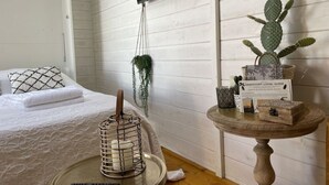 Une chambre avec un lit, une plante suspendue, un téléviseur fixé au mur, un cactus posé sur une table et une télécommande sur un plateau.