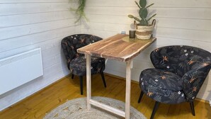 Une pièce d’angle avec une table en bois, deux chaises à motifs, une plante suspendue et un cactus dans un panier tressé.