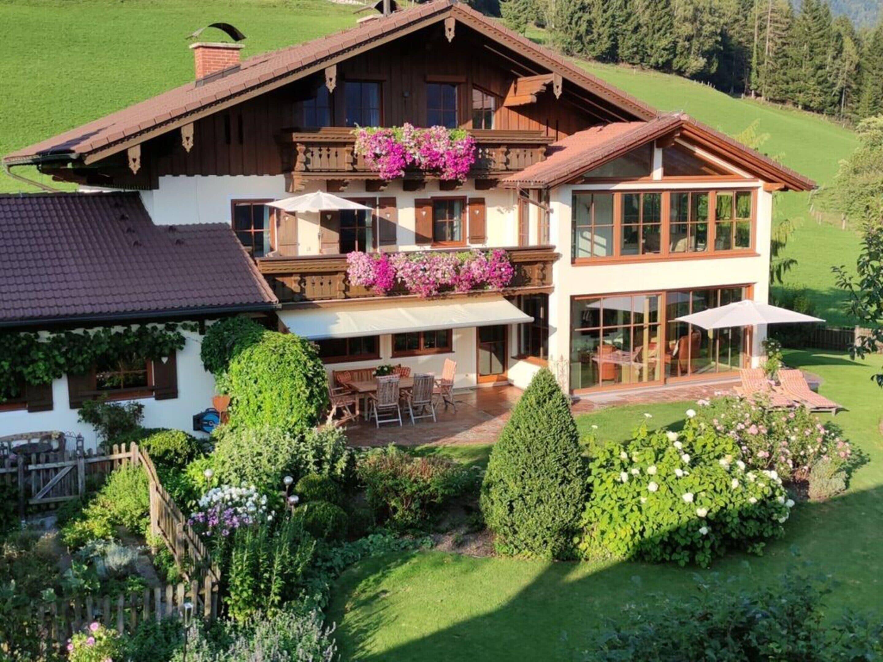 A two-story chalet with a balcony, a patio with outdoor furniture, and a well-maintained garden.