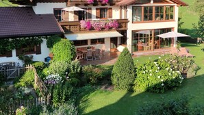 A two-story chalet with a balcony, a patio with outdoor furniture, and a well-maintained garden. - Holiday Apartment The Neuhaus (Abtenau)