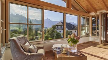 A spacious room with large windows offering a mountain view, a leather sofa, and a wooden coffee table.