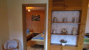 Una habitación de madera con una cama litera, una mesita pequeña, una estantería con adornos y una silla.