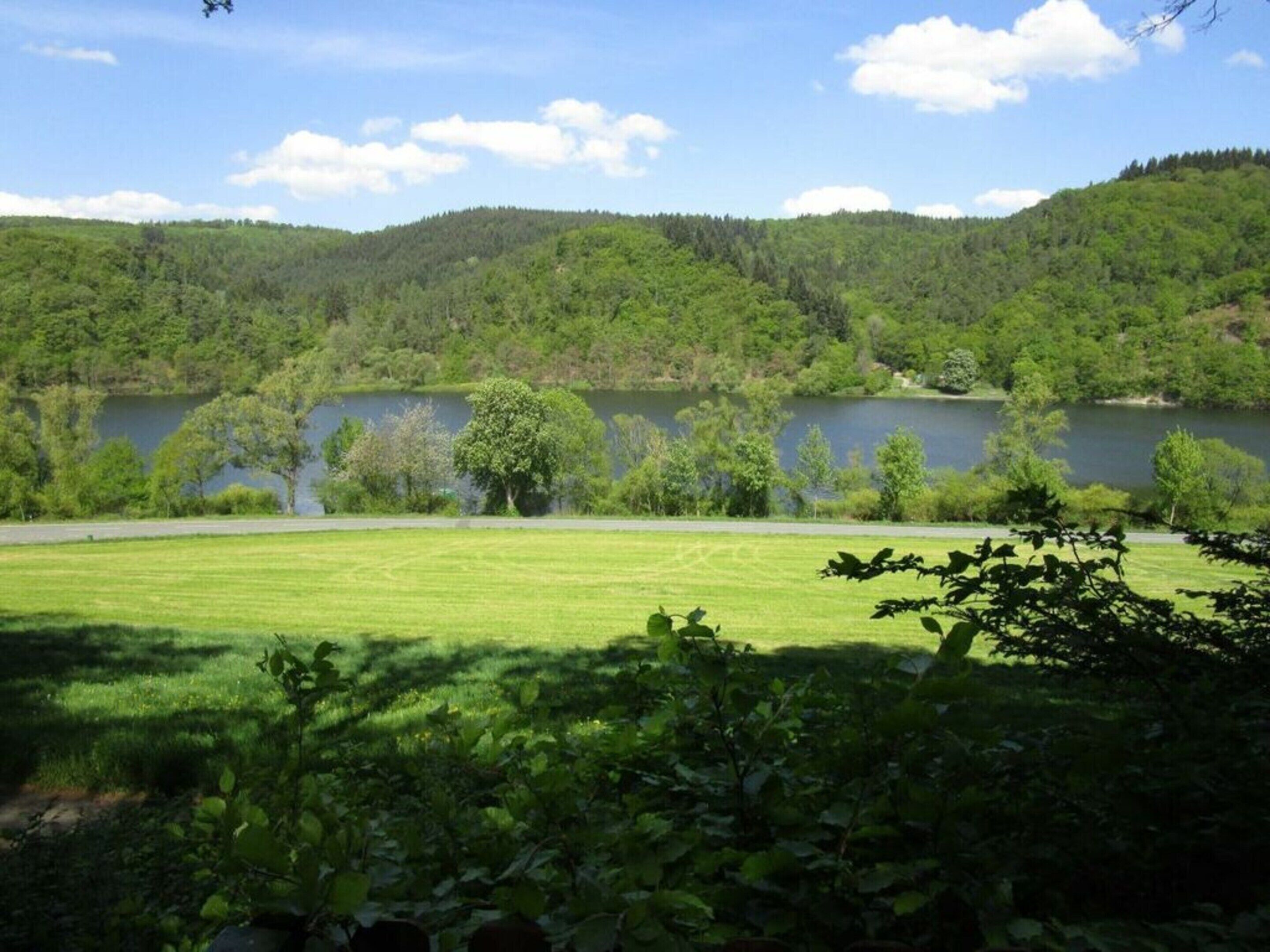 A serene landscape with a lake, lush green hills, and a well-maintained grassy area.