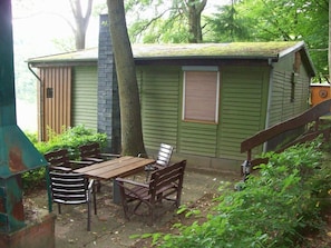 A small cabin with a chimney, a window with blinds, and a wooden table with chairs.