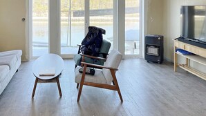 A modern living room with a white sofa, a round coffee table, and a wooden chair. There is a TV on a wooden stand and a heater on the floor. - 8 Person Holiday Home in Seim (Alver)