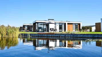 A modern house with a glass facade, a wooden deck, and a pond in front.