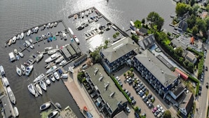 Vue aérienne d’une marina avec des bateaux amarrés, un parking et des bâtiments adjacents.