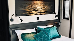 Une chambre à coucher avec un lit, deux oreillers, une table de chevet et une lampe fixée au mur.
