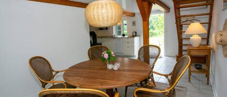 Zona pranzo con tavolo rotondo in legno circondato da sedie in vimini, lampada a sospensione in vimini e cucina sullo sfondo.