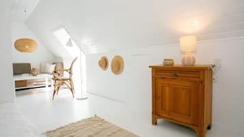 Une pièce avec un plafond en pente, une armoire en bois, une lampe en osier, un tapis tissé et un présentoir à chapeaux fixé au mur.