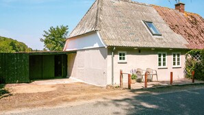 A single-story house with a sloped roof, a small porch with chairs, and a fenced garden area.