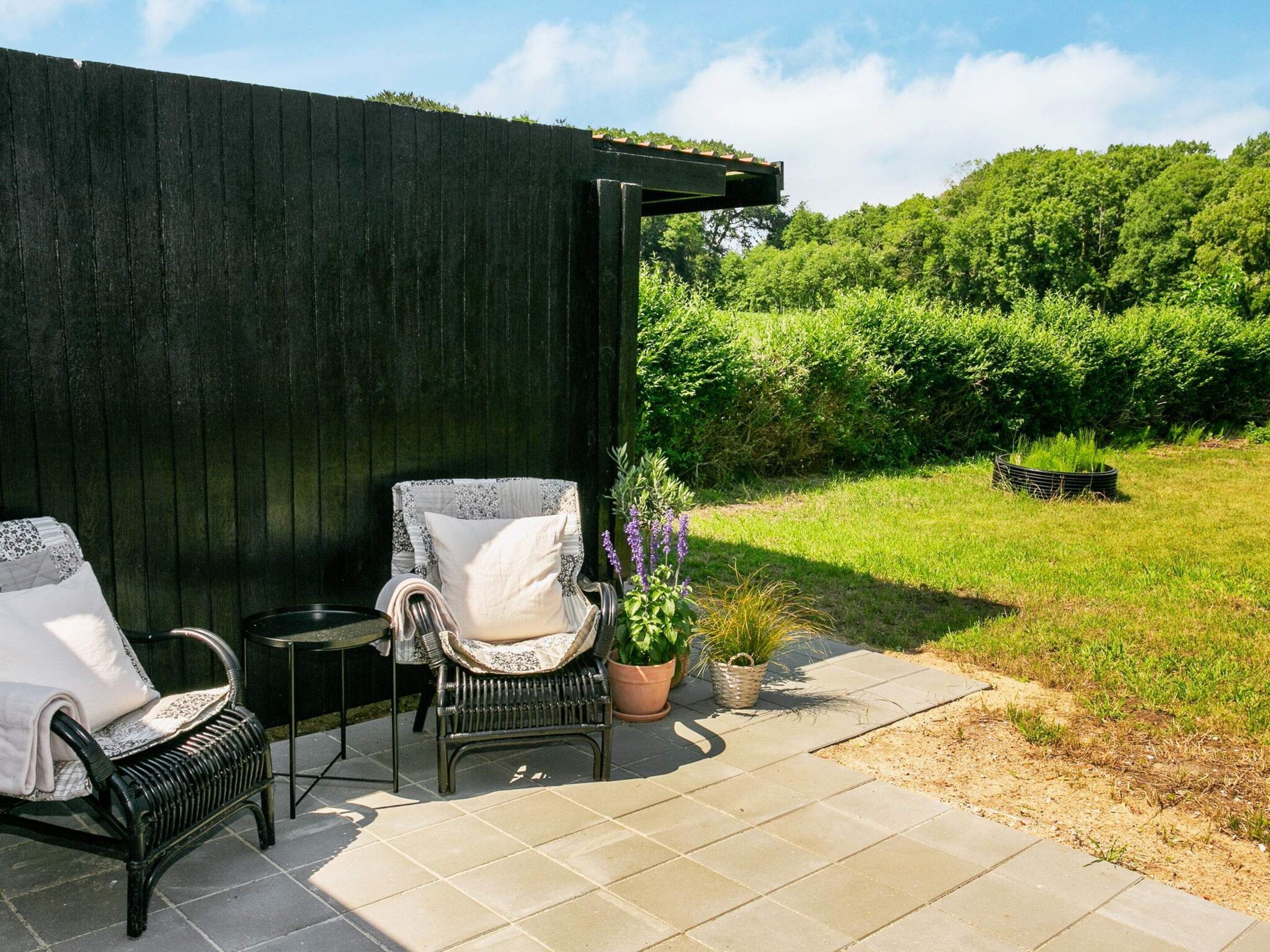 Een terras met twee rieten stoelen en een kleine tafel, omringd door een donker houten hek en weelderig groen.
