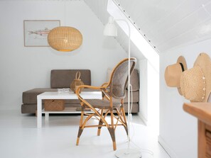 A modern living room with a white sofa, a wicker chair, a white table, and a hanging lamp. - 4 Person Holiday Home in Rudkobing (Rudkobing)