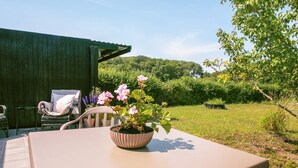An outdoor patio with a table and chairs, a potted plant with flowers, and a view of a green landscape.