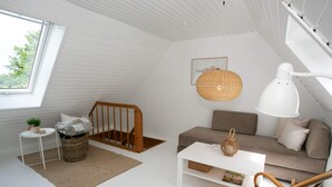A modern loft bedroom with a sloped ceiling, a white sofa, a wicker chair, a white coffee table, and a large window. - 4 Person Holiday Home in Rudkobing (Rudkobing)