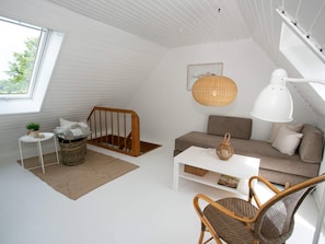 A modern loft bedroom with a sloped ceiling, a white sofa, a wicker chair, a white coffee table, and a large window. - 4 Person Holiday Home in Rudkobing (Rudkobing)