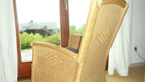 Un fauteuil à bascule en osier, doté d’un siège et d’un dossier rembourrés, placé devant une porte-fenêtre coulissante donnant sur un balcon.