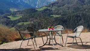 Une table et des chaises sont disposées sur une terrasse en pierre, avec vue sur la montagne.
