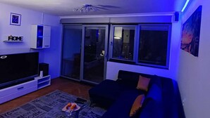A living room with a flat-screen TV, a sofa, a coffee table with oranges, and a newspaper mat. - Apartment Sunrise (Dugi Rat)