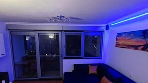 A living room with a dark blue sofa, a glass door leading to an outdoor area, and a ceiling light fixture. - Apartment Sunrise (Dugi Rat)
