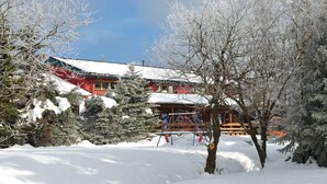 A snow-covered landscape with a red building featuring a wooden deck and snow-covered trees. - Rasehorn Comfortable Holiday Residence (Altenberg)