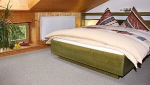 A bedroom with a wooden ceiling, a bed with multiple pillows, a radiator, and a window with a view of trees. - Rasehorn Comfortable Holiday Residence (Altenberg)